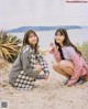 A couple of young women sitting on top of a sandy beach.