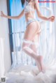 A woman in a white lingerie and fishnet stockings posing on a bed.