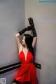 A woman in a red dress and black gloves leaning against a wall.