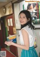 A woman in a white top and blue skirt holding a book.