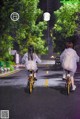 A couple of people riding bikes down a street in the rain.