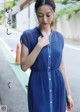 A woman in a blue dress is standing on the street.