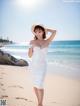 A woman in a white dress and hat on the beach.