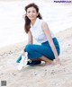 A woman kneeling on the beach with a pair of flip flops.